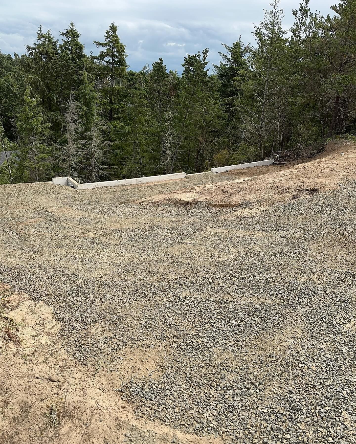 Gravel path curving through a forested hillside under a partly cloudy sky