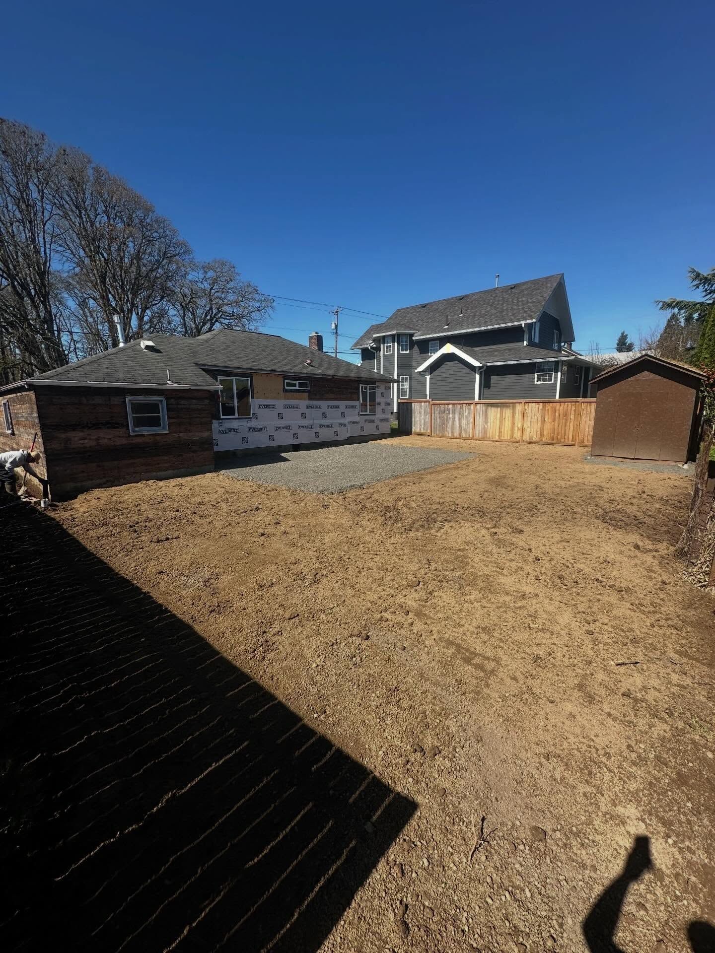 Backyard with dry grass, wooden sheds, and a house under a clear blue sky