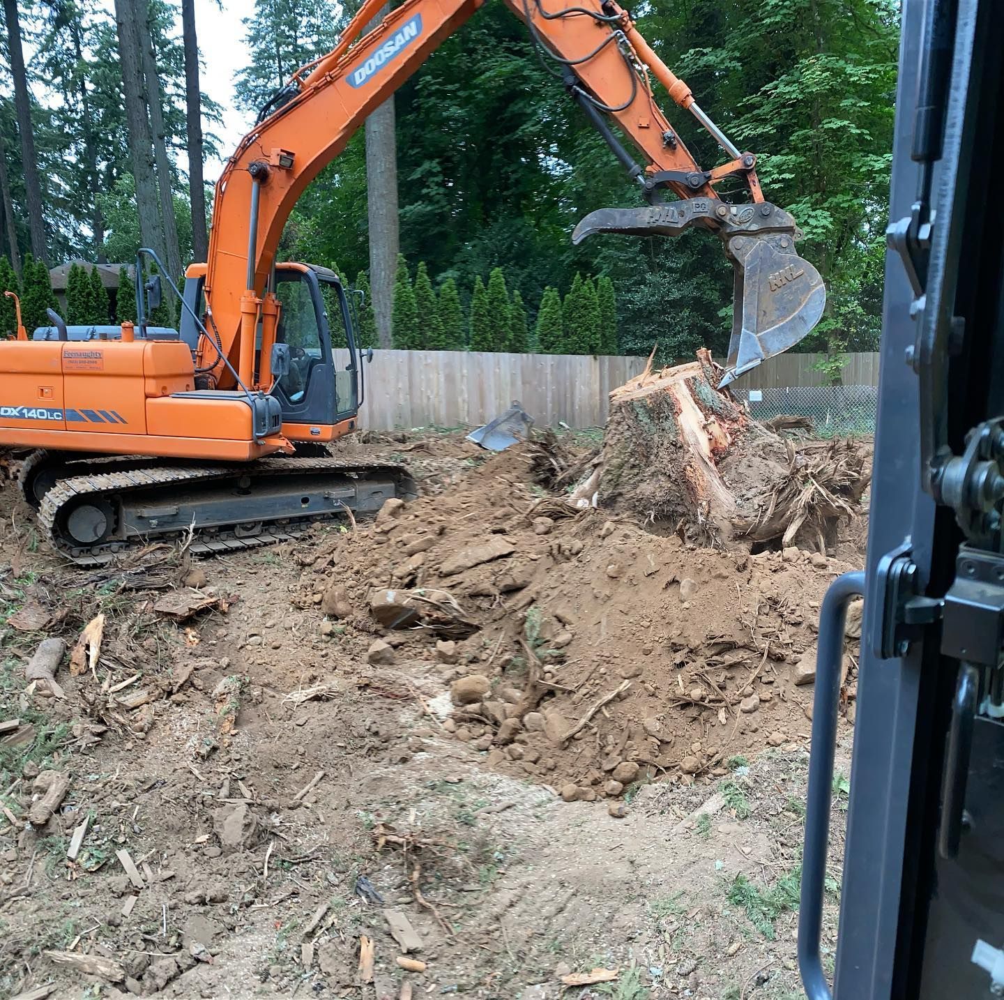 Orange excavator digging soil beside a fence in a wooded area