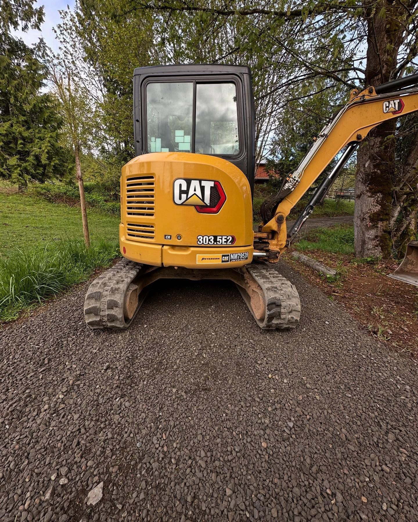 Yellow CAT excavator on a gravel path beside trees and grass.