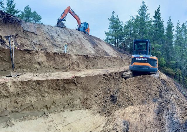 Excavator and dump truck working on a steep dirt hillside in a forest clearing