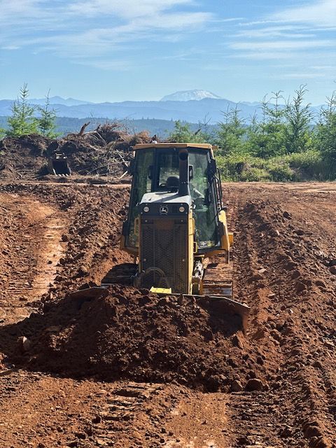 Yellow backhoe digging soil on a dirt road with mountains in the background