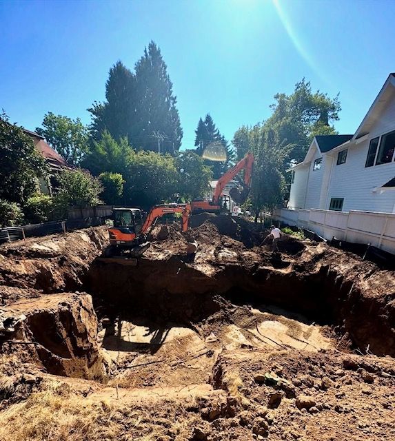 Large excavation pit with an orange excavator beside a white house on a sunny residential street