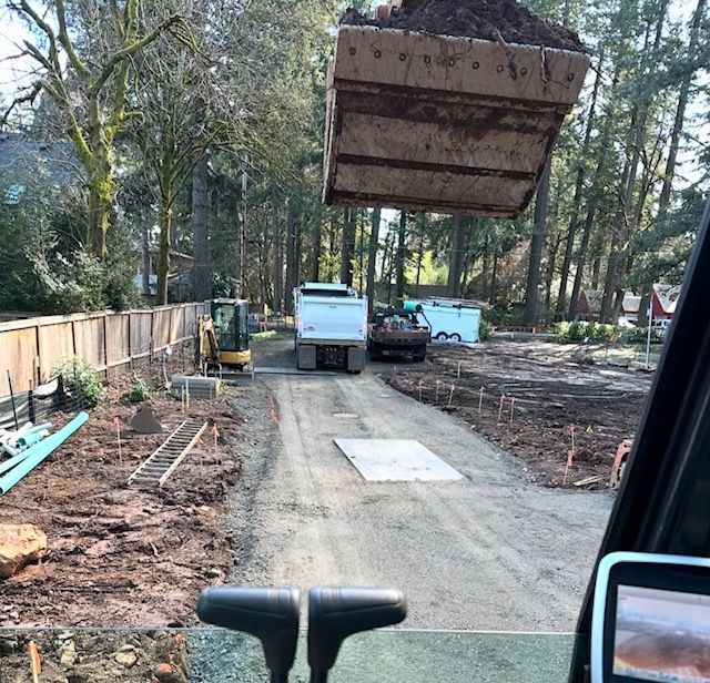 Construction site with a truck and excavator on a dirt driveway in a wooded area