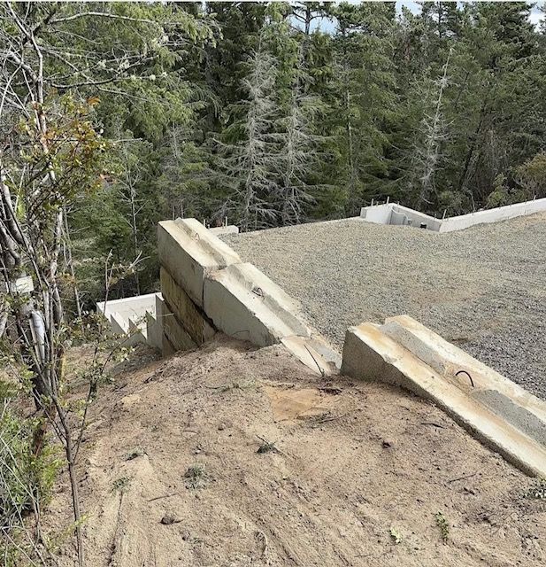 Damaged concrete roof edge beside a wooded hillside, with debris and exposed construction material