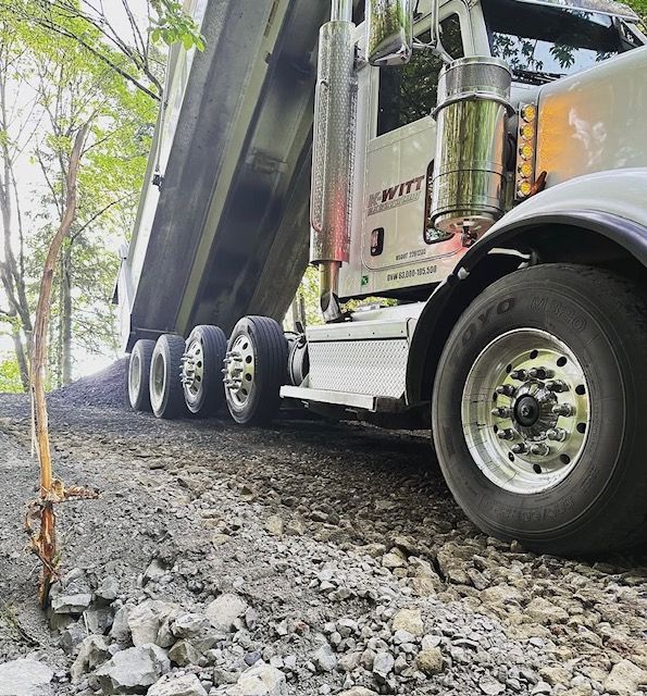 Large dump truck hauling gravel on a rough road, low-angle view of rear wheels and bed