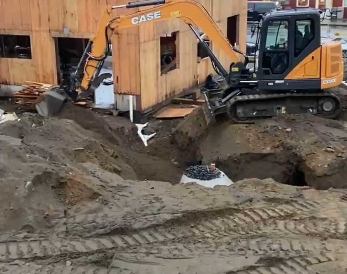 Orange excavator digging soil at a construction site beside a wooden house under construction.