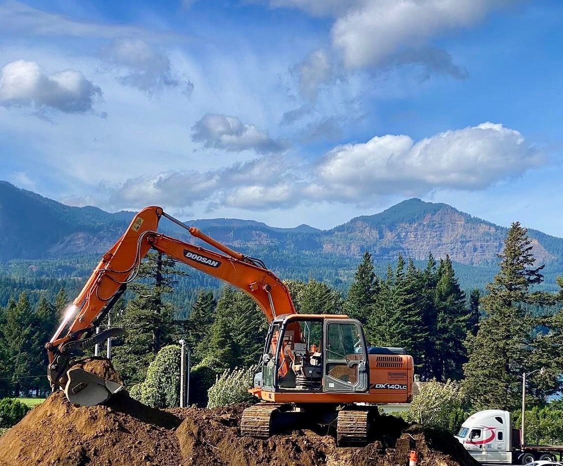 Orange excavator digging dirt at a construction site with mountains and trees in the background