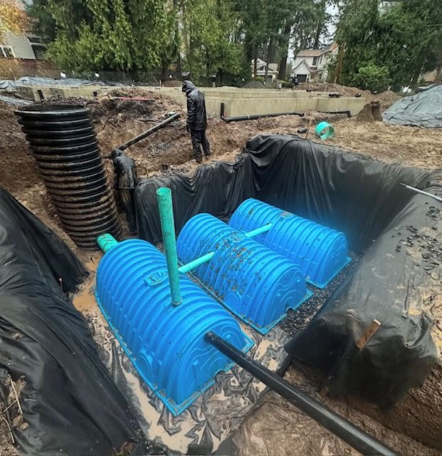 Blue underground drainage tanks installed in a trench, with black lining and a worker standing nearby.