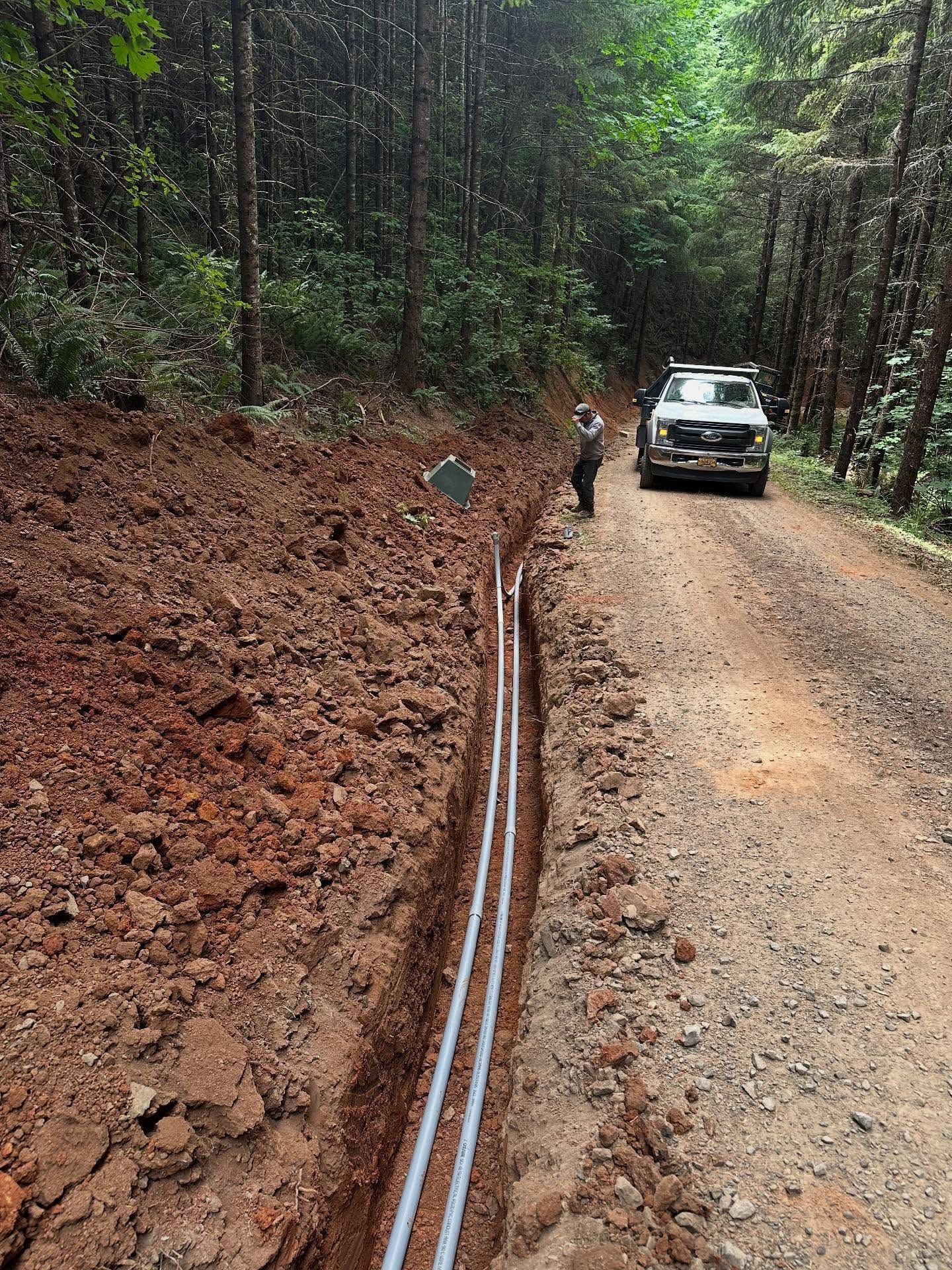 Freshly laid blue pipeline in a muddy forest roadside trench beside a dirt road and parked SUV