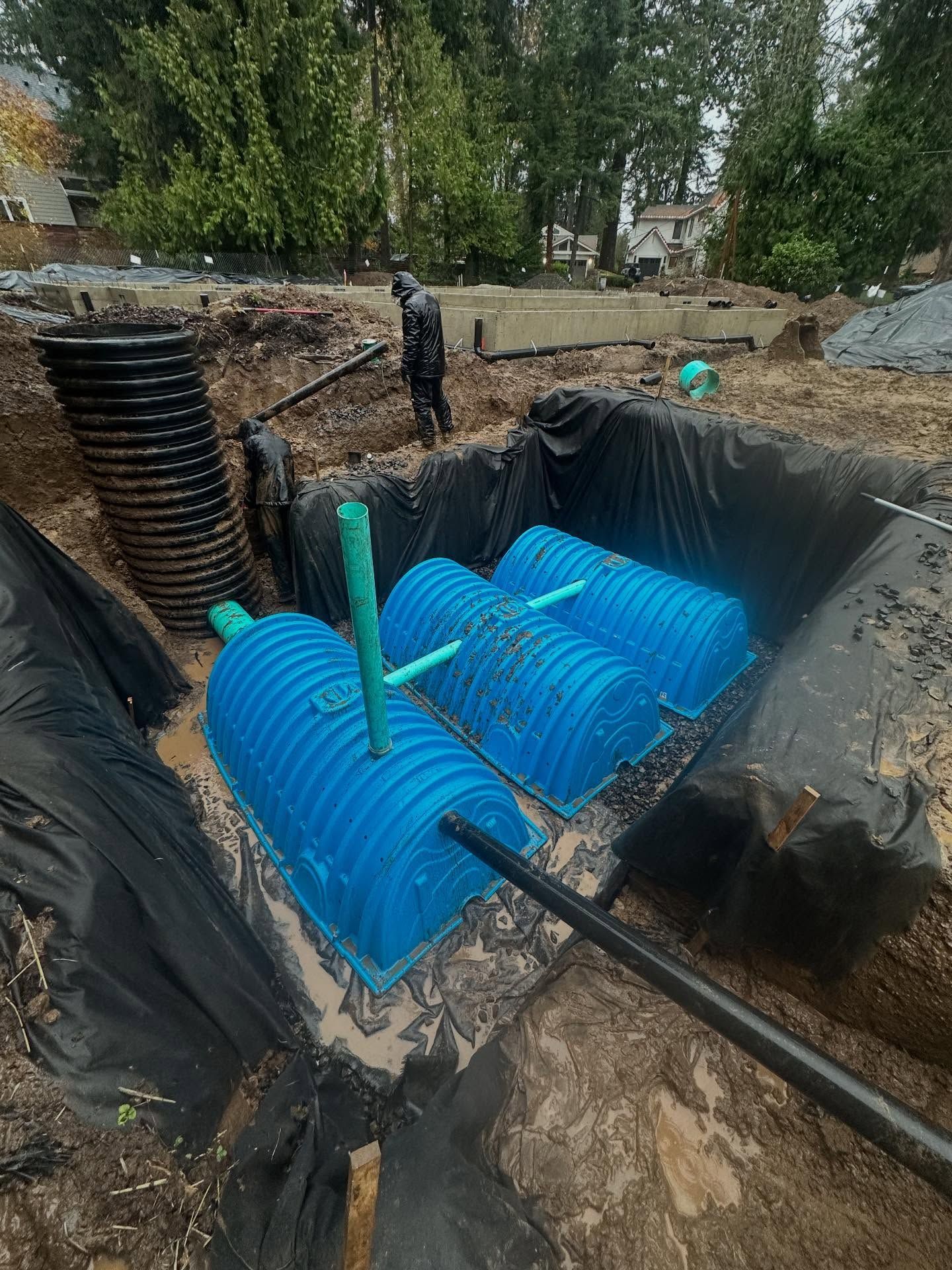 Construction site with blue underground tanks in a pit, black liner, and a worker nearby