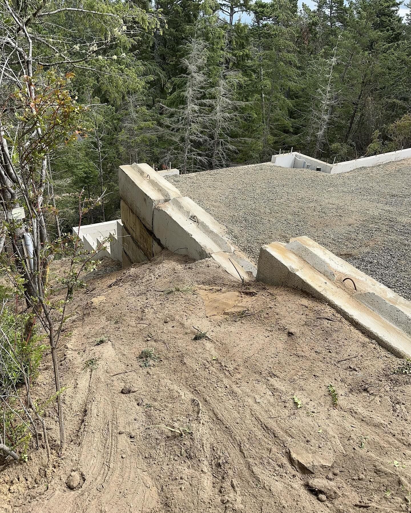 Gravel-covered ramp or roadway edge with broken concrete slabs beside trees and brush
