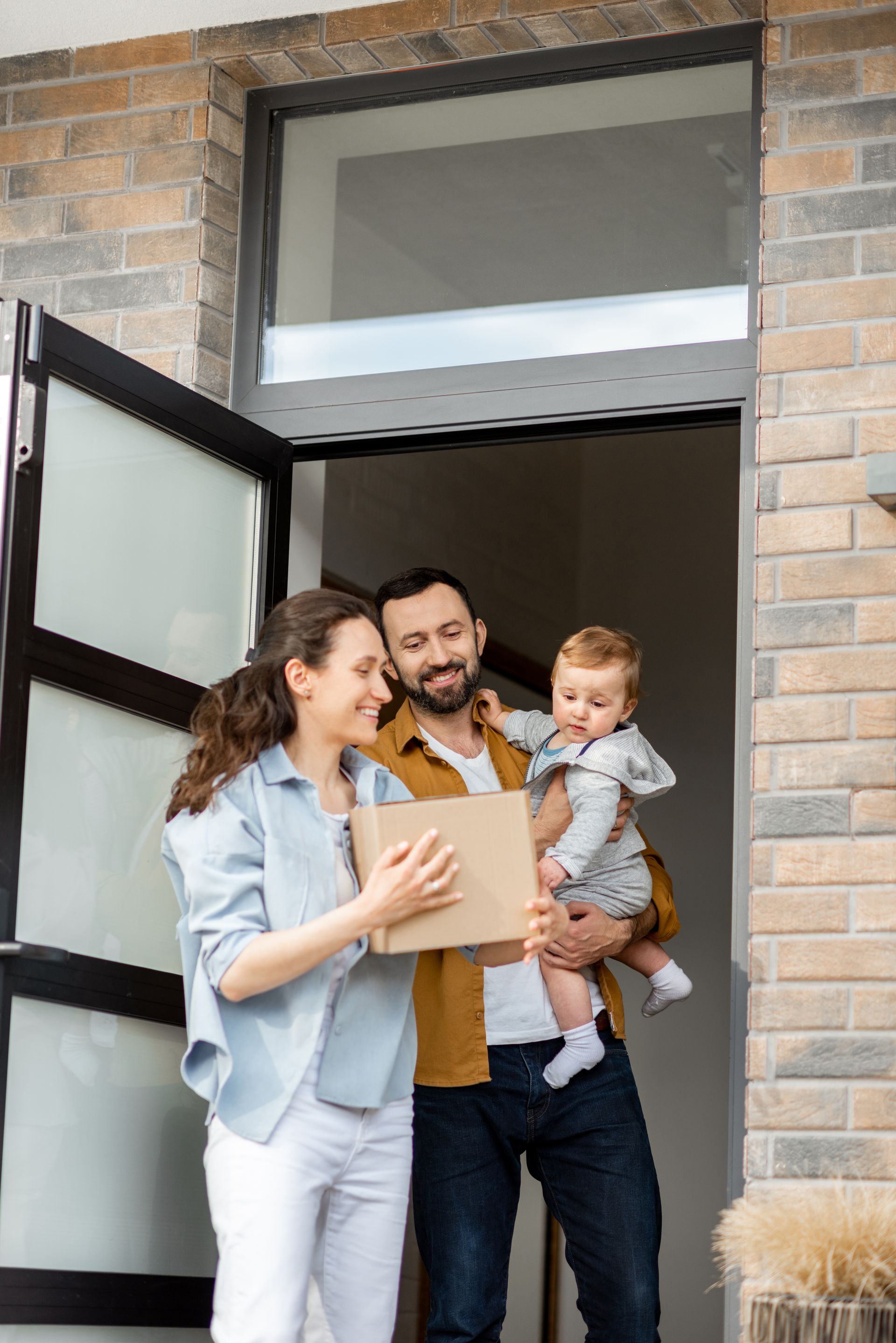 Family carrying boxes at an open front door during a move