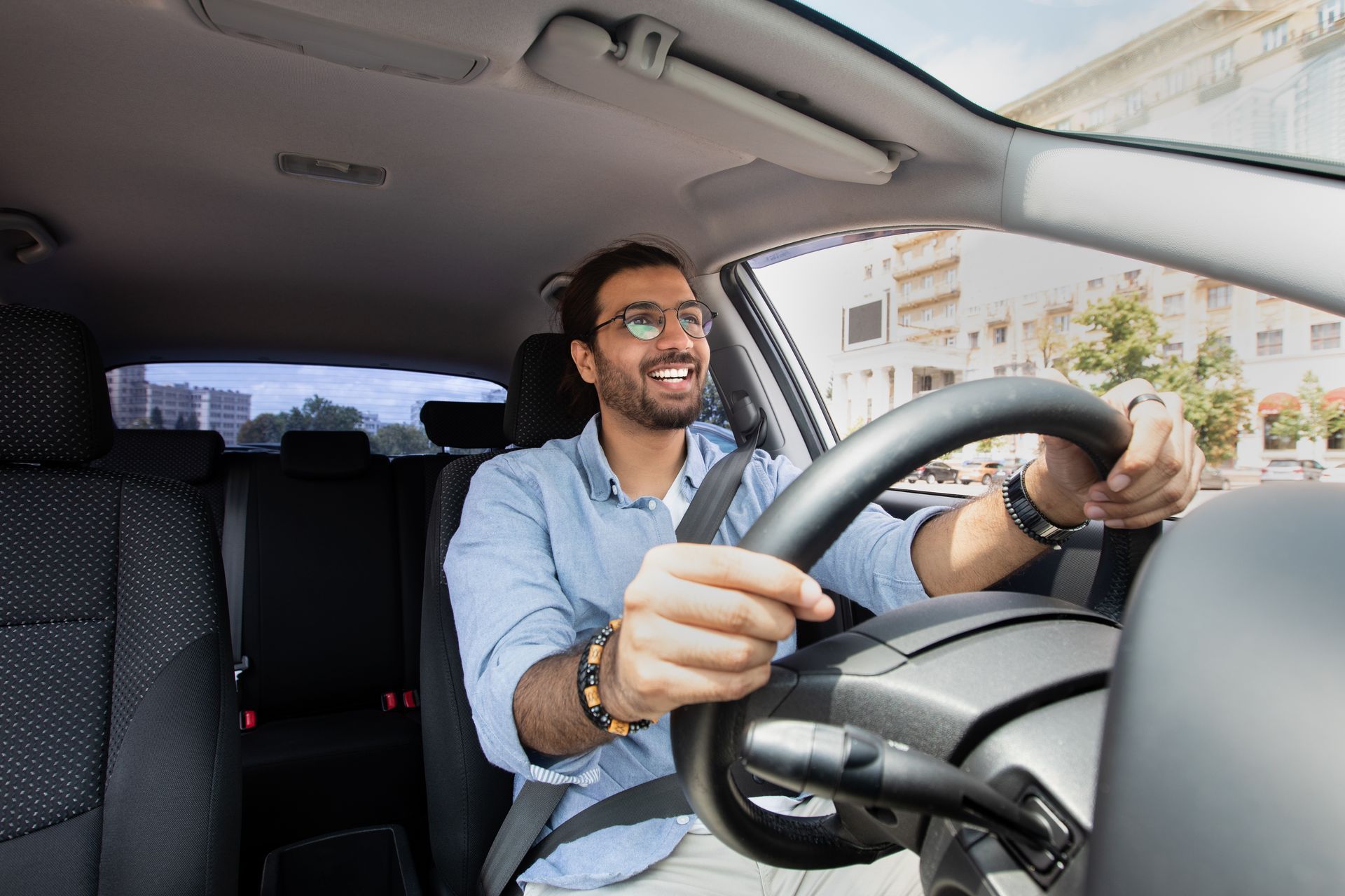 Smiling driver in sunglasses and blue shirt steering a car interior