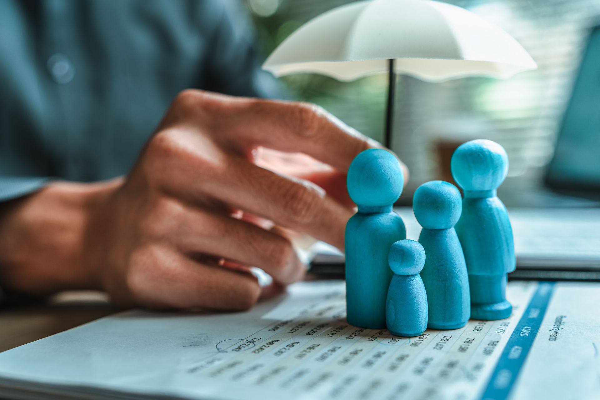 Blue toy figures beside a hand on documents under an umbrella at a desk