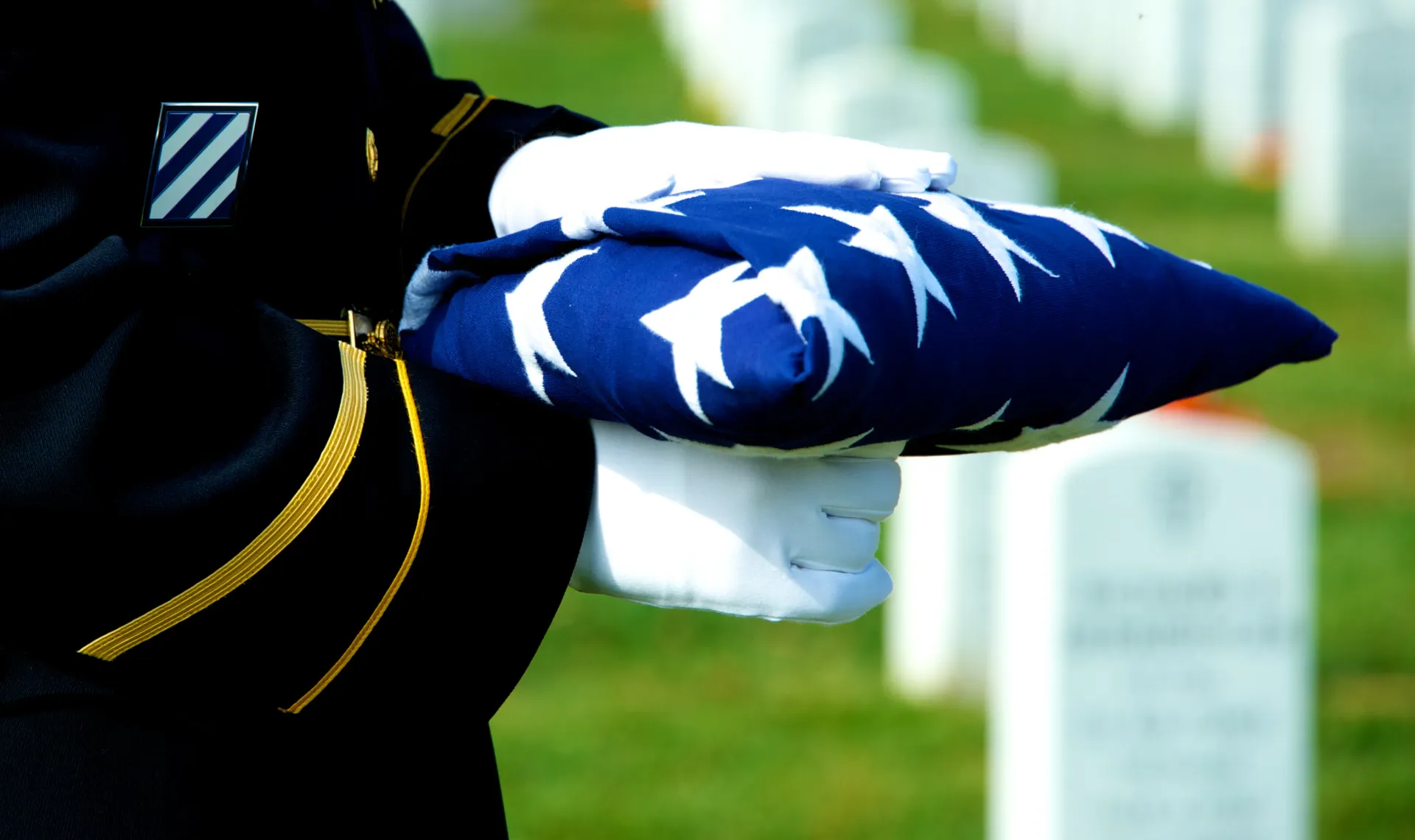 A soldier is holding an american flag in front of a cemetery