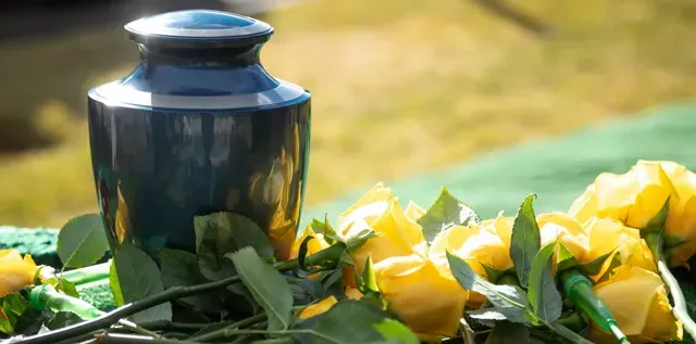 A blue urn sitting on top of a table next to yellow roses.