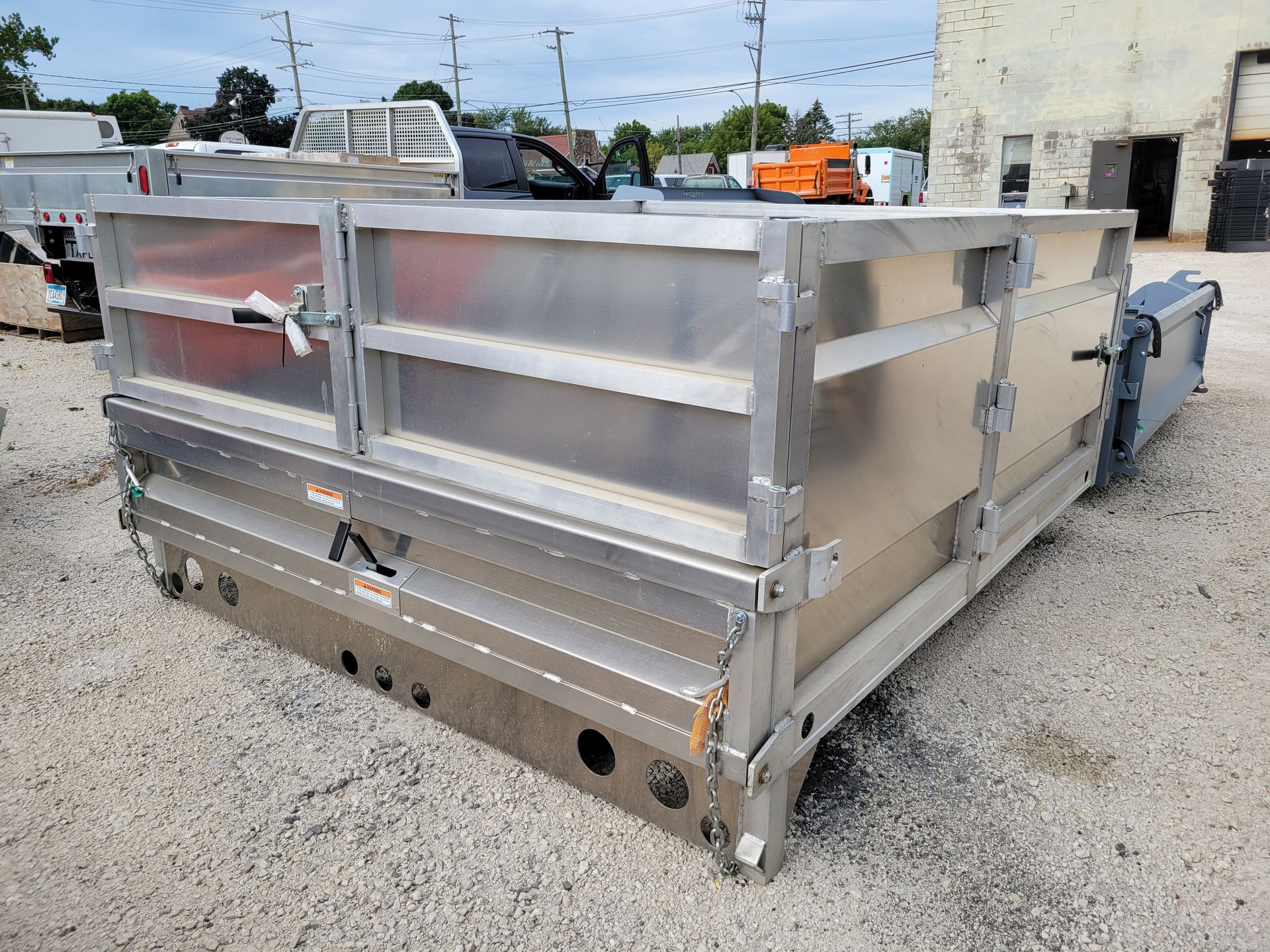 A large aluminum dumpster is parked in a gravel lot in front of a building.