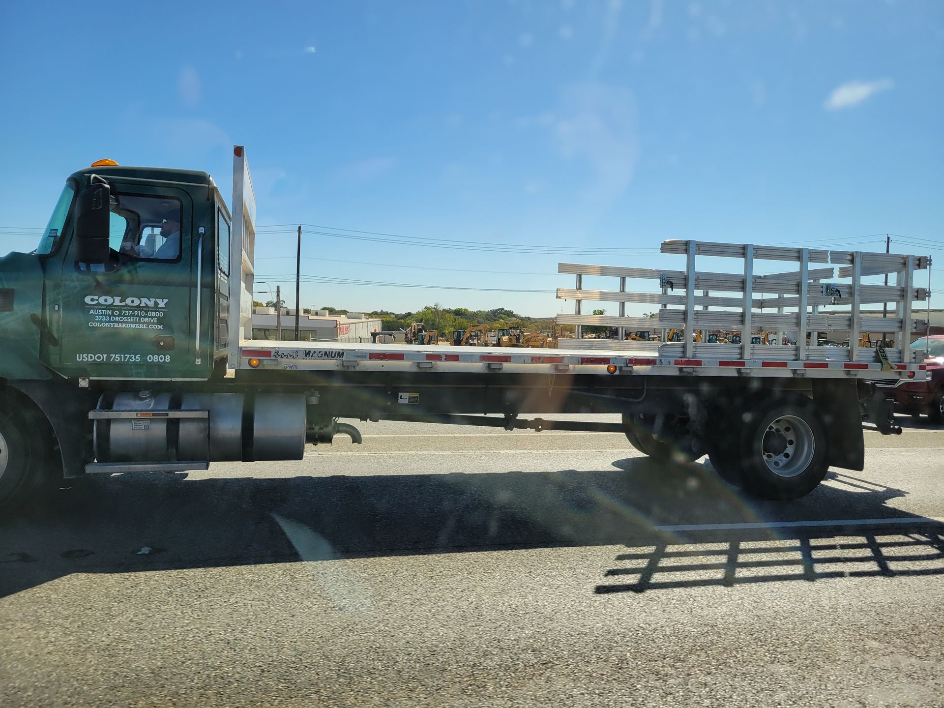 A green truck with a flatbed is parked on the side of the road