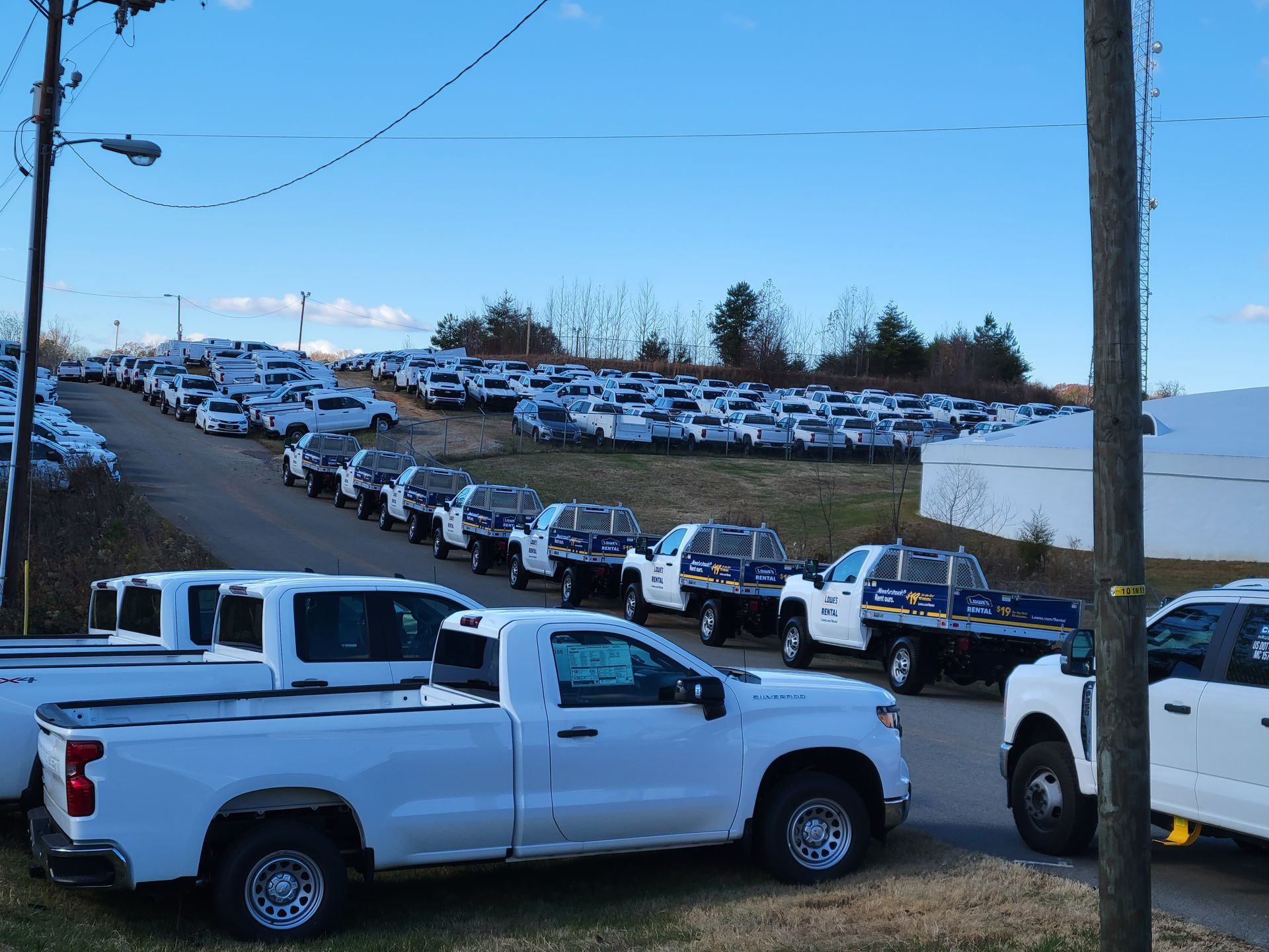 A lot of white trucks are parked on the side of the road.