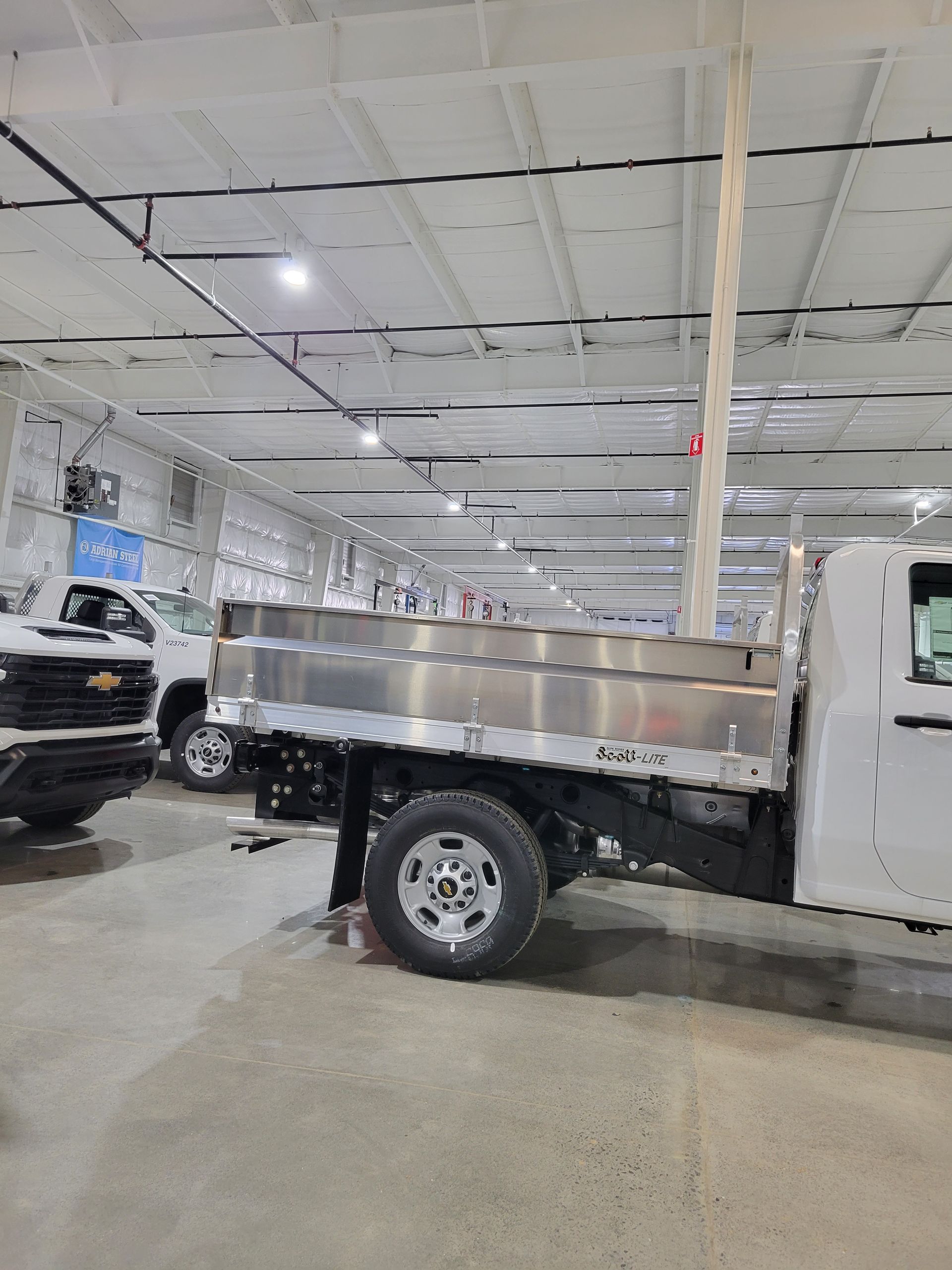 A white truck is parked in a warehouse next to a black truck.