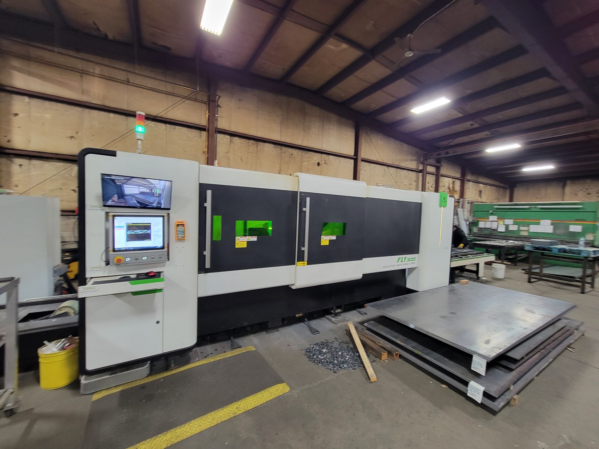 A large machine is sitting in a warehouse next to a stack of metal sheets.