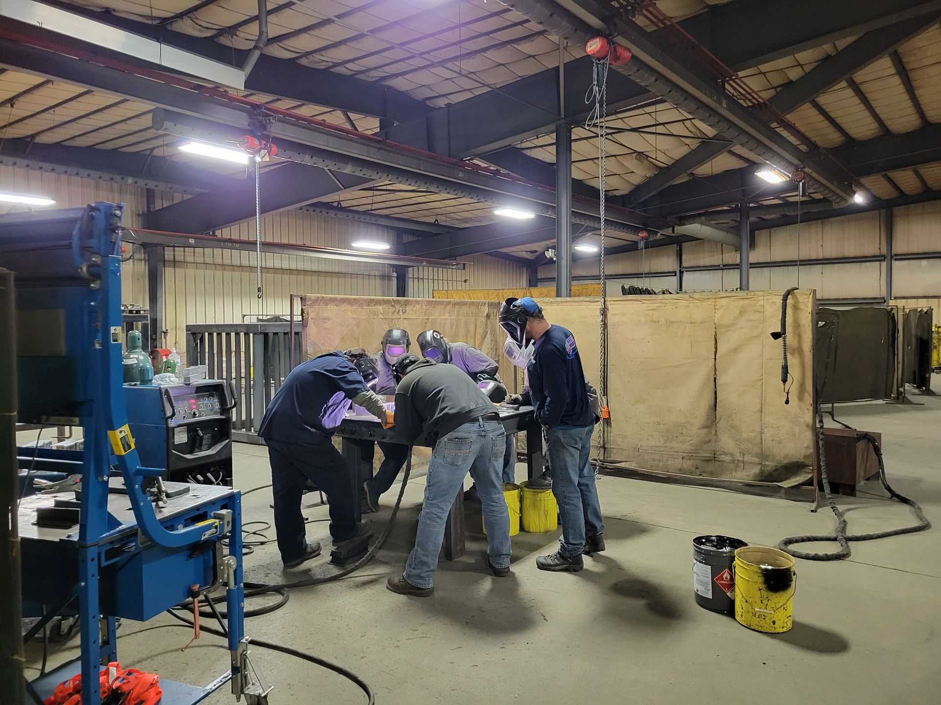 A group of men are welding in a large warehouse.