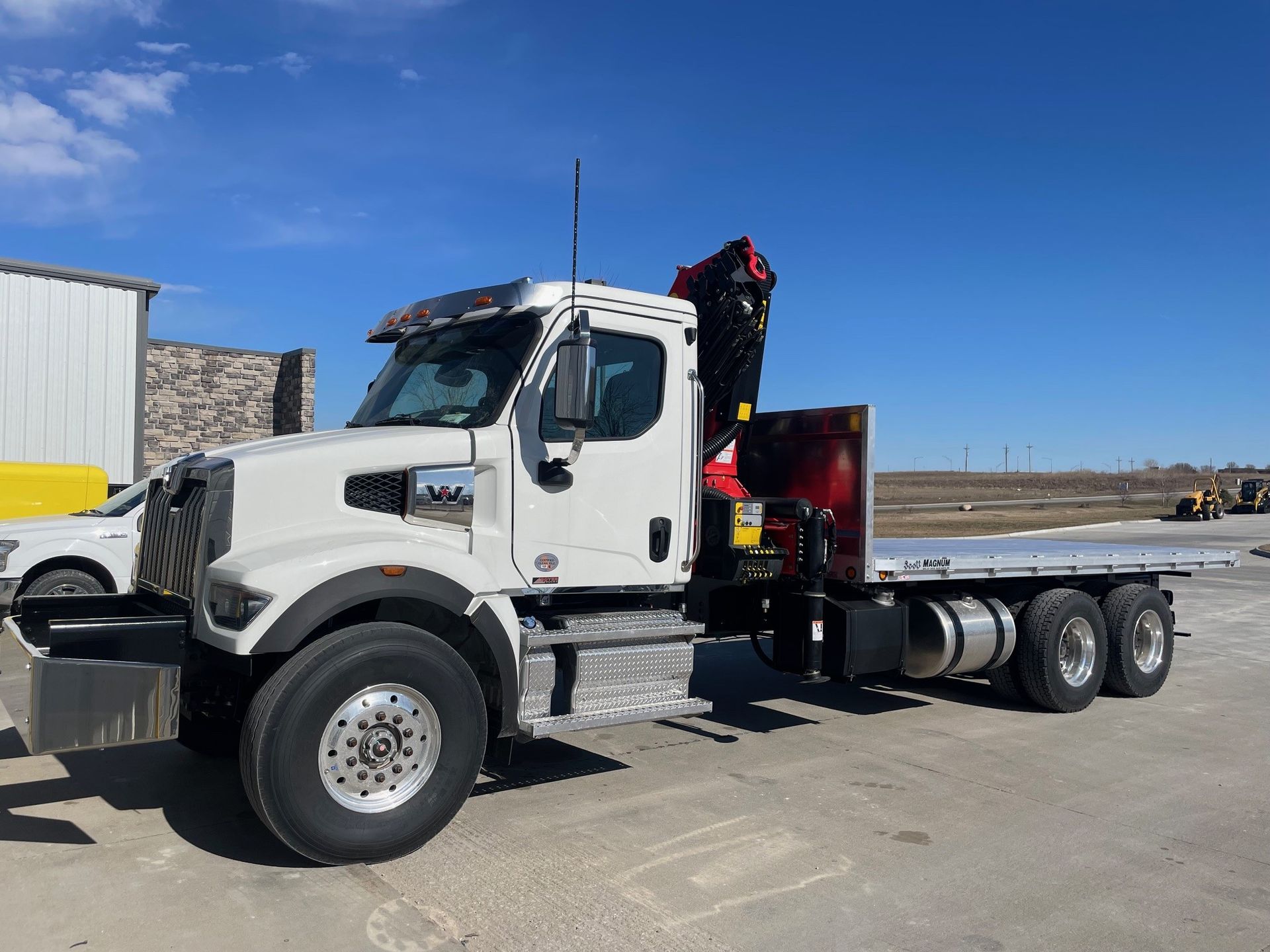 A white flatbed truck with a crane attached to it is parked in a parking lot.