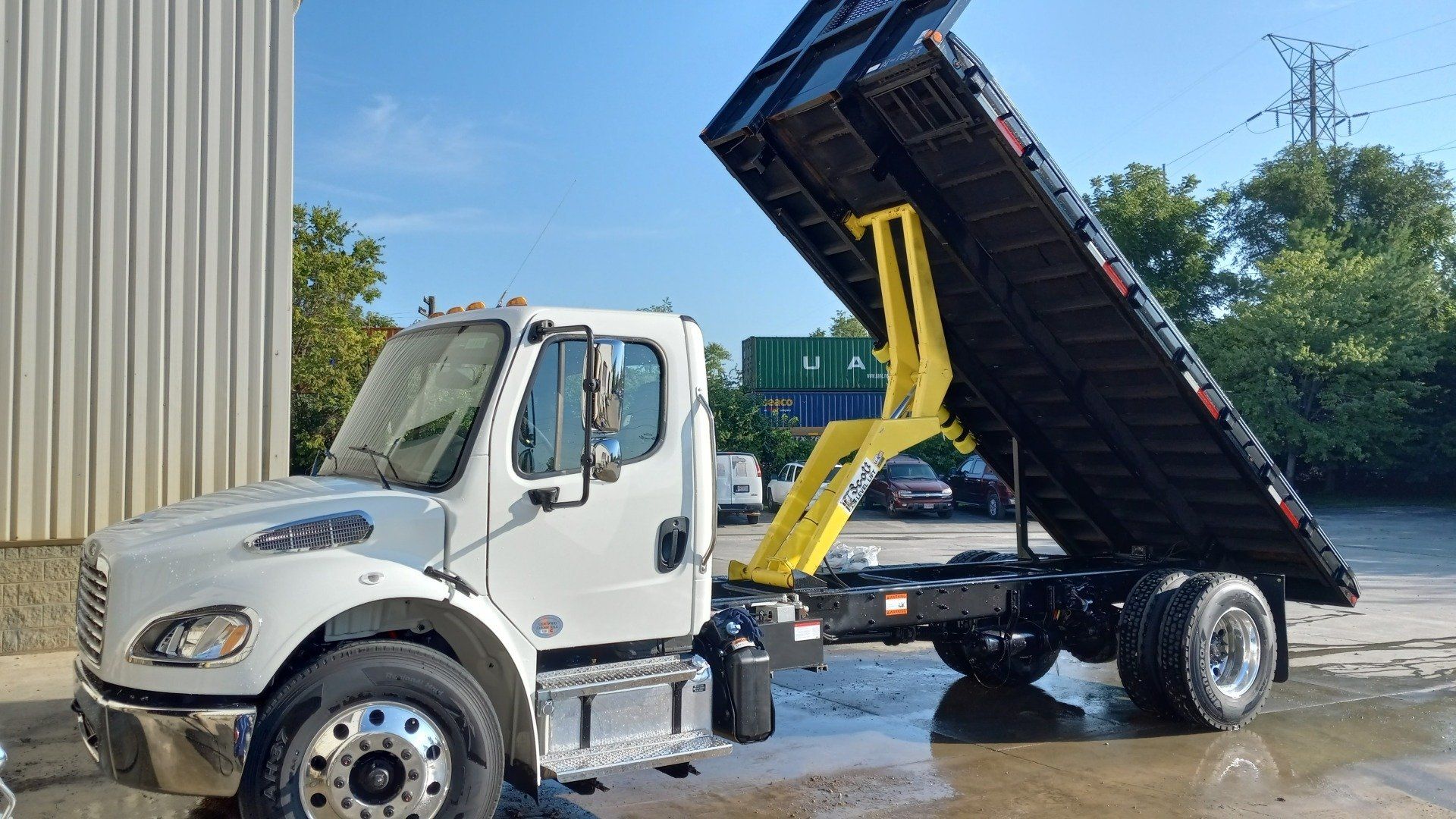 A white dump truck with a yellow crane on the back is parked in a parking lot.