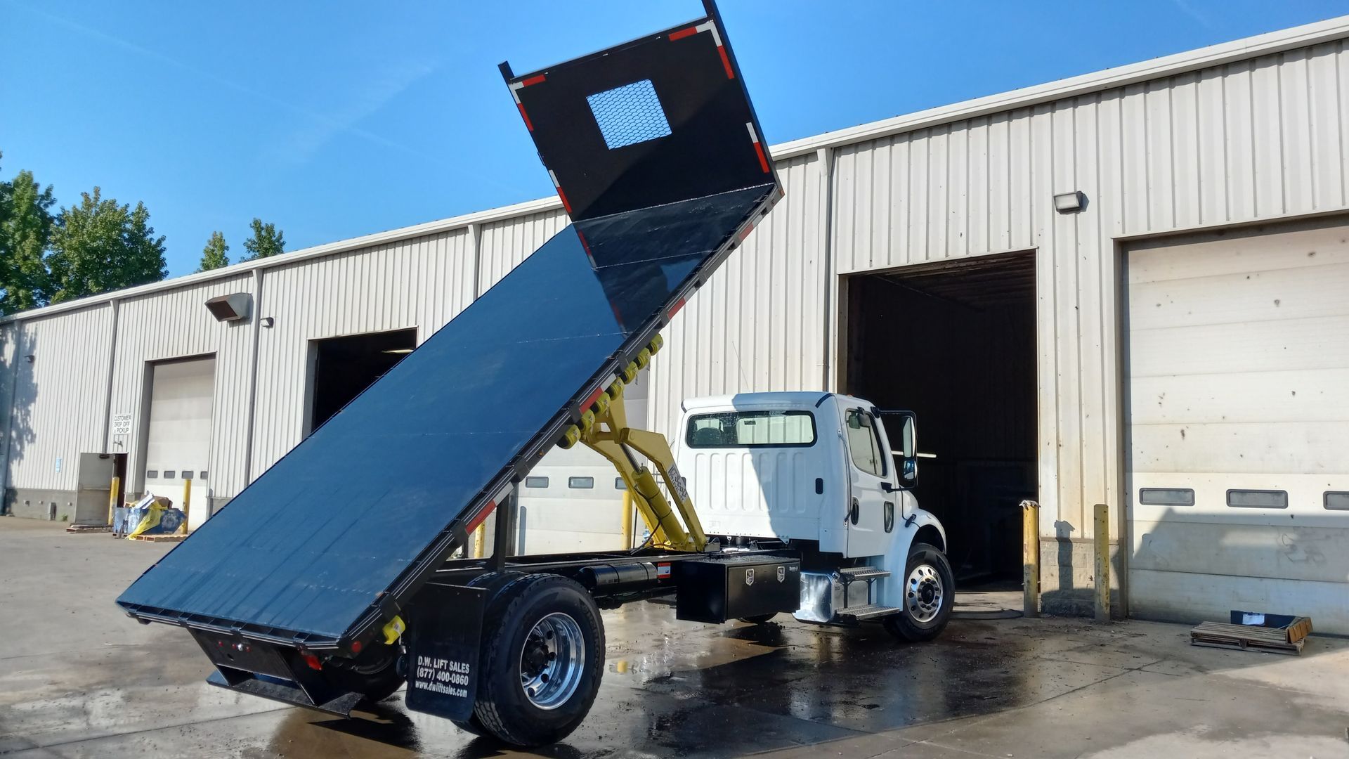 A dump truck with its bed up is parked in front of a building.
