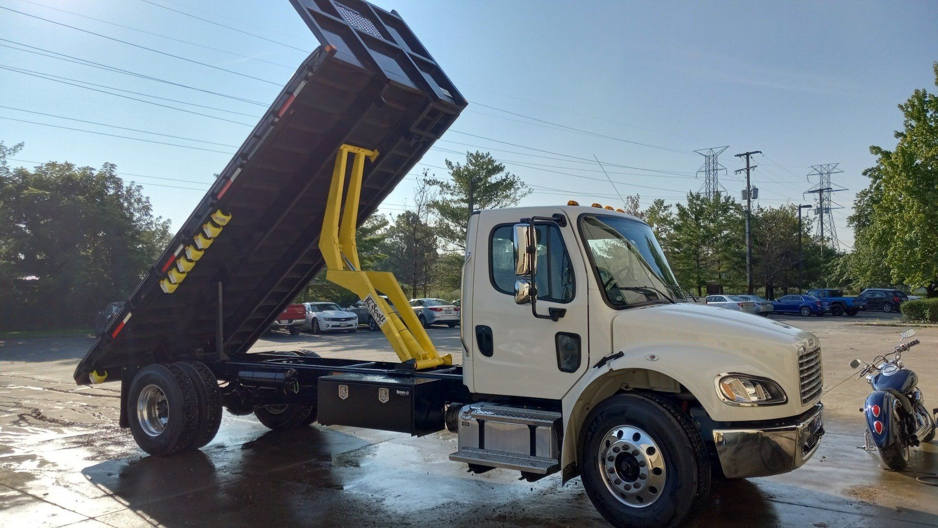 A dump truck is parked in a parking lot next to a motorcycle.