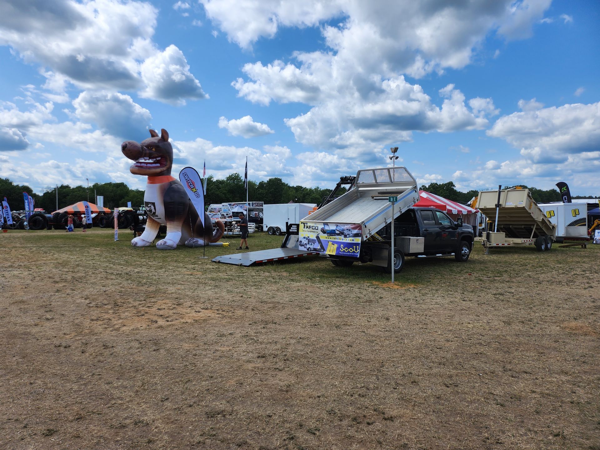 A large inflatable dog is sitting next to a truck in a field.