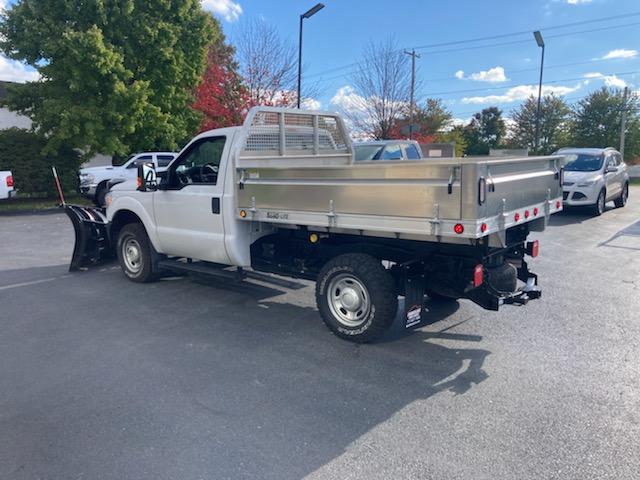 A white truck with a snow plow attached to it is parked in a parking lot.
