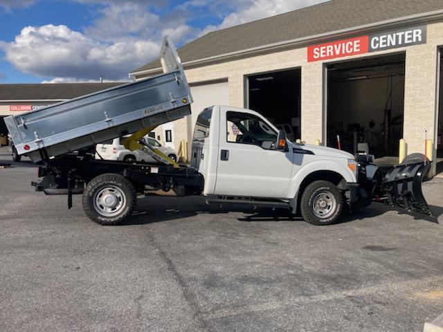 A white dump truck with a snow plow attached to it is parked in front of a service center.
