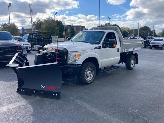 A white truck with a snow plow attached to it is parked in a parking lot.