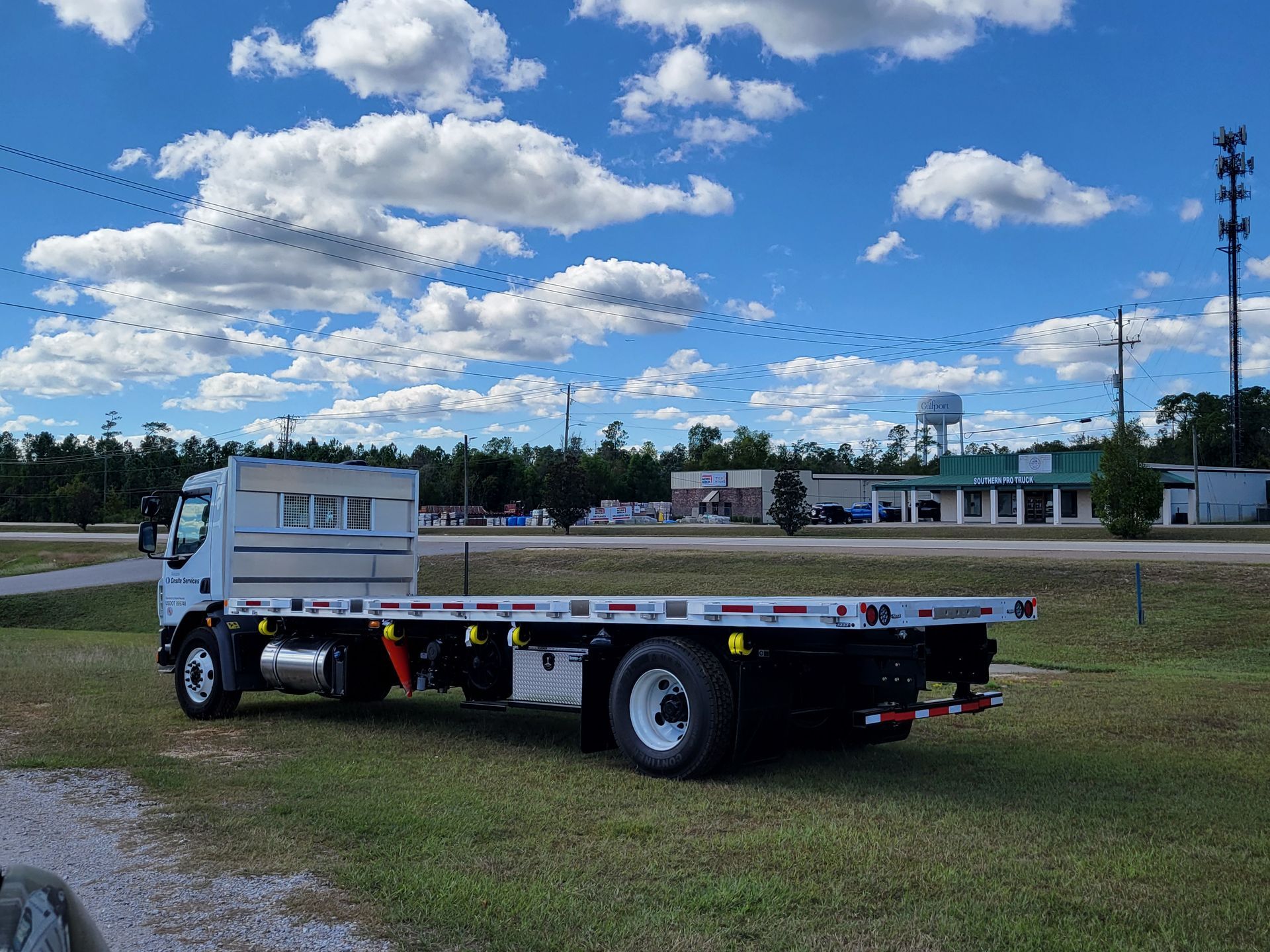 A flatbed tow truck is parked in a grassy field.