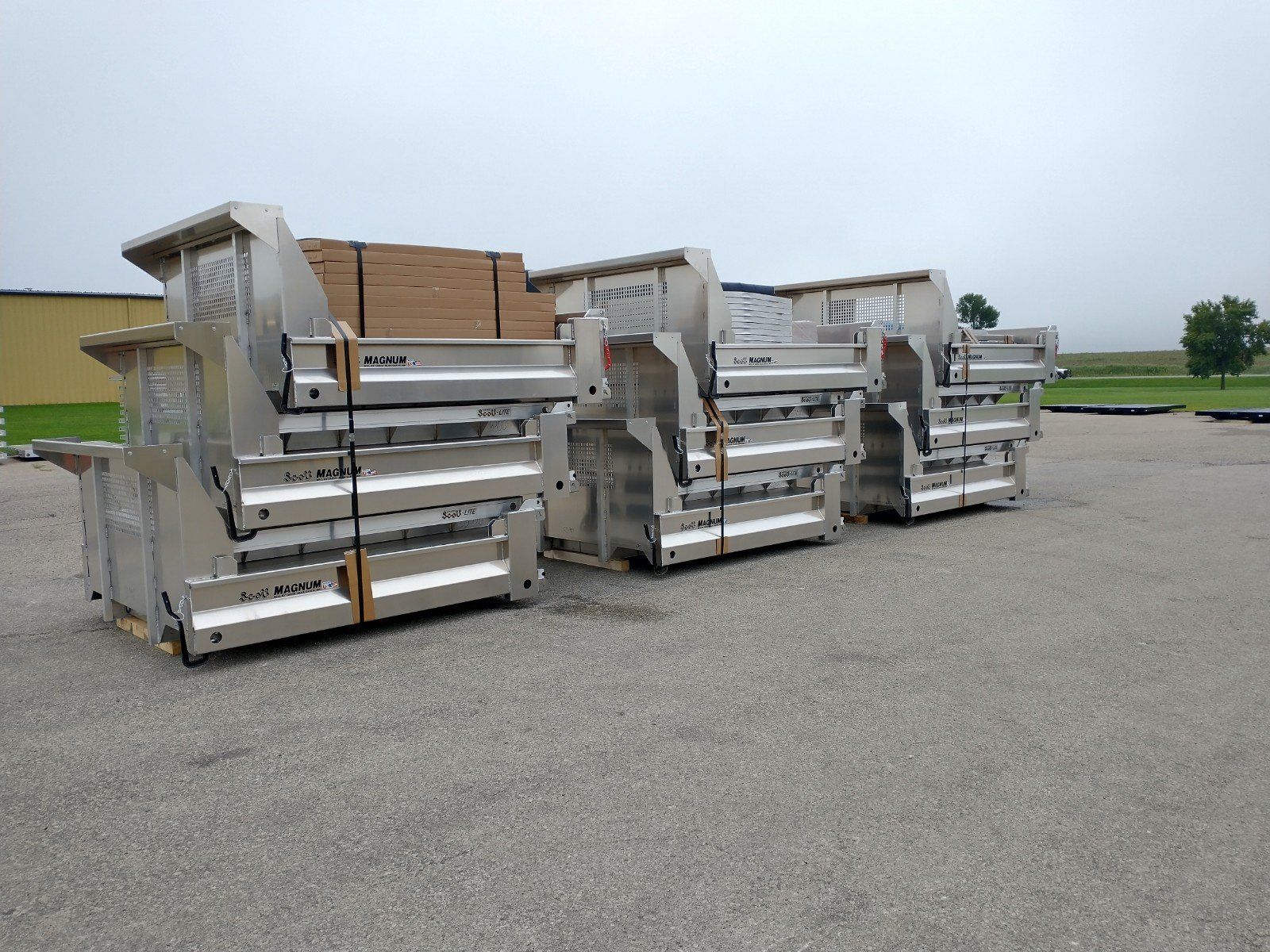 A row of stainless steel dumpsters are lined up in a parking lot.