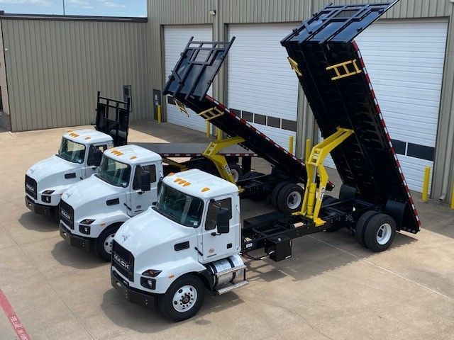 Three dump trucks are parked next to each other in front of a garage.