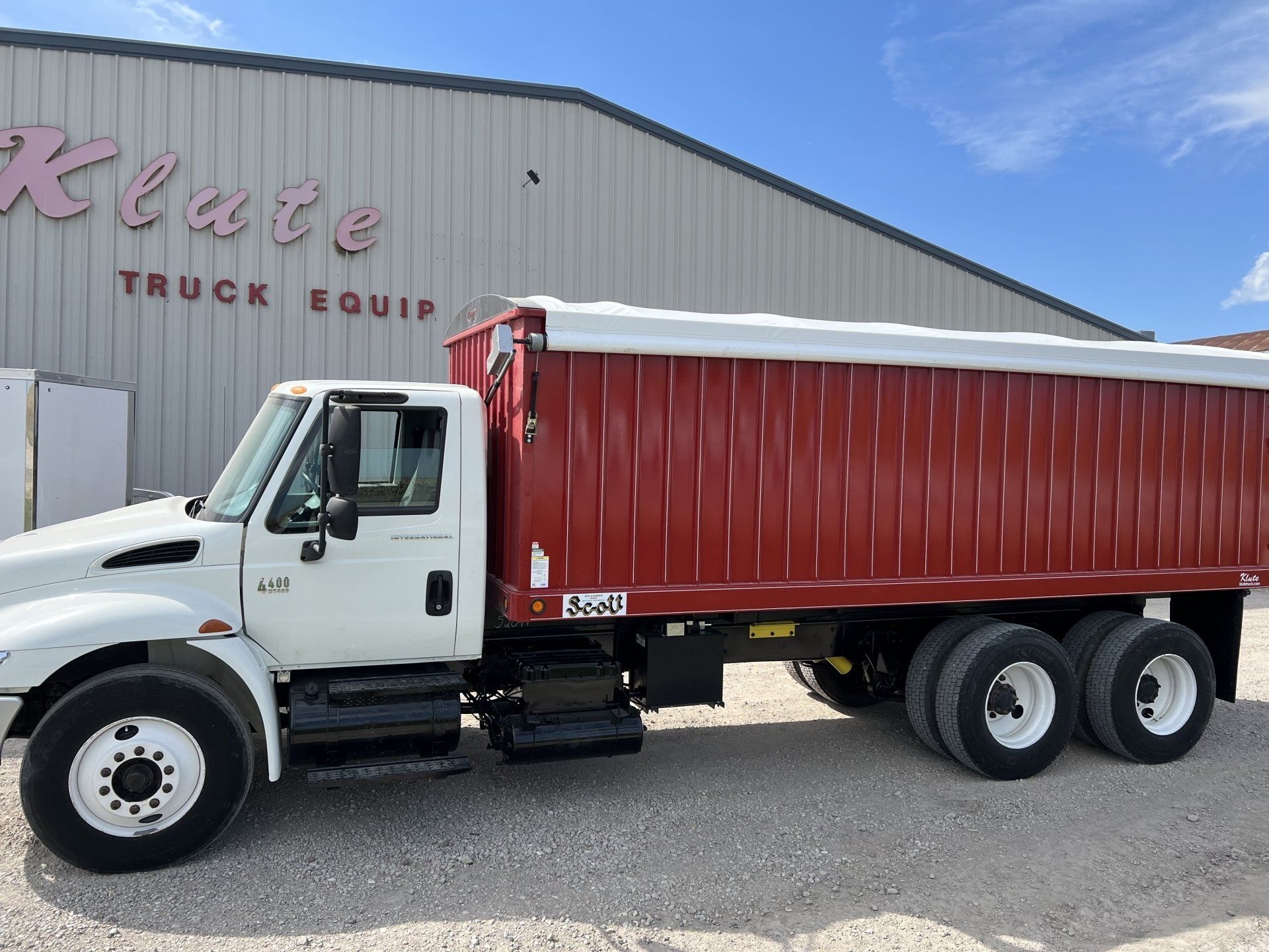 A white truck with a red trailer is parked in front of a building.