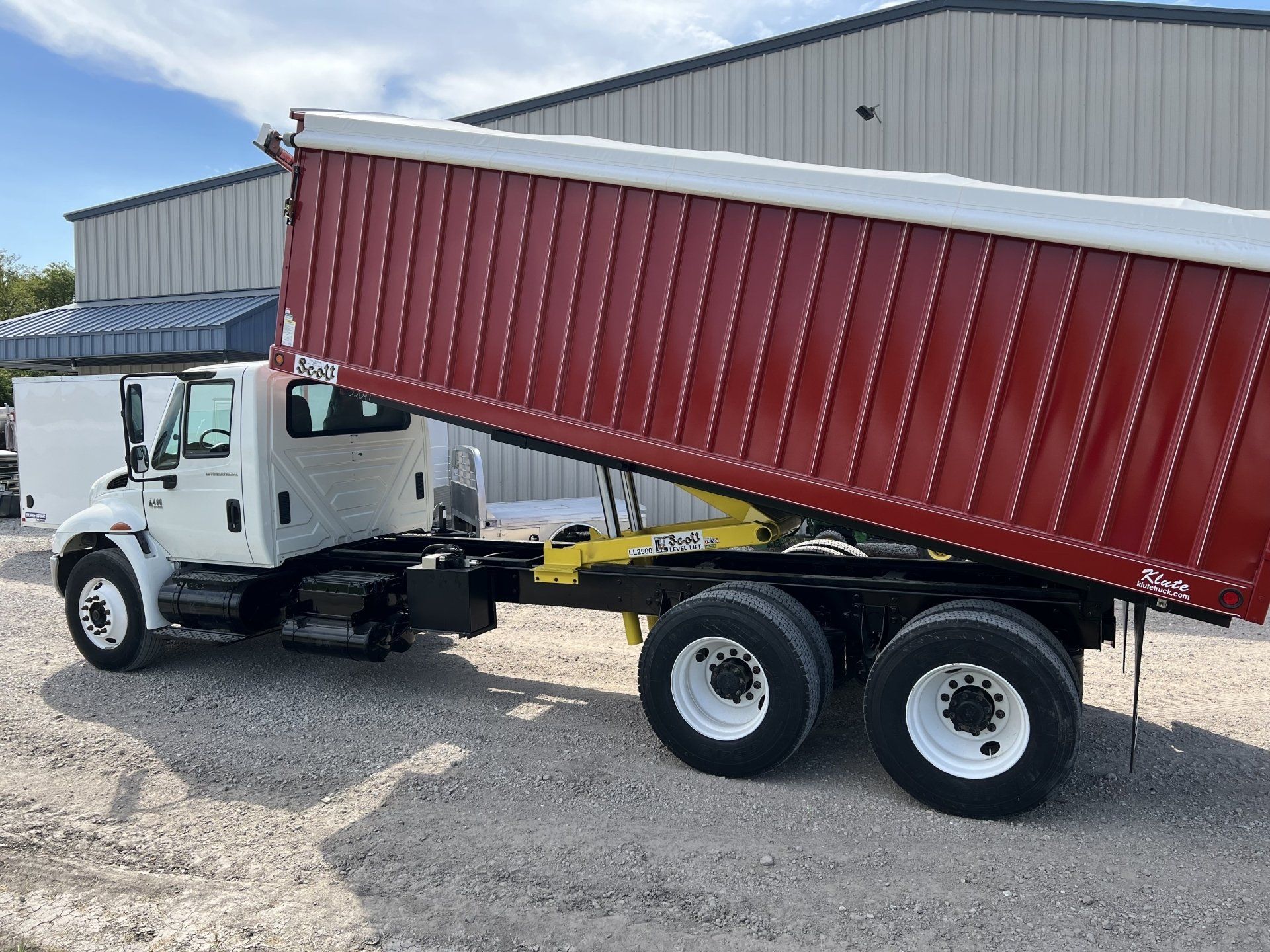 A white dump truck with a red trailer is parked in front of a building.