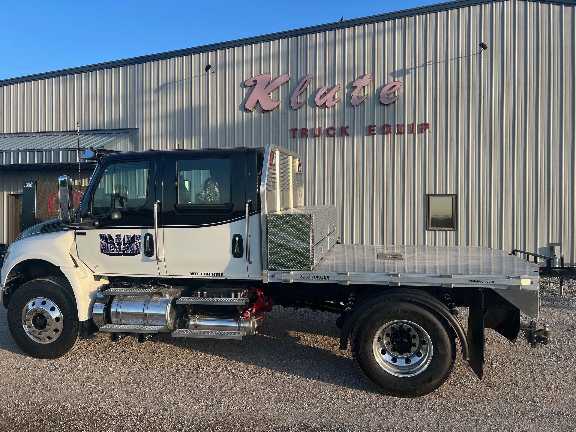 A white flatbed truck is parked in front of a building.