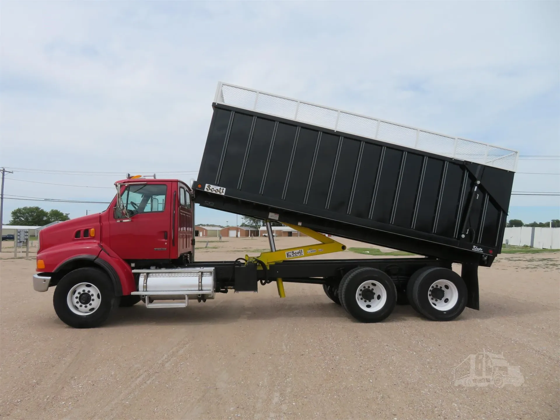 A red dump truck is parked in a dirt field.