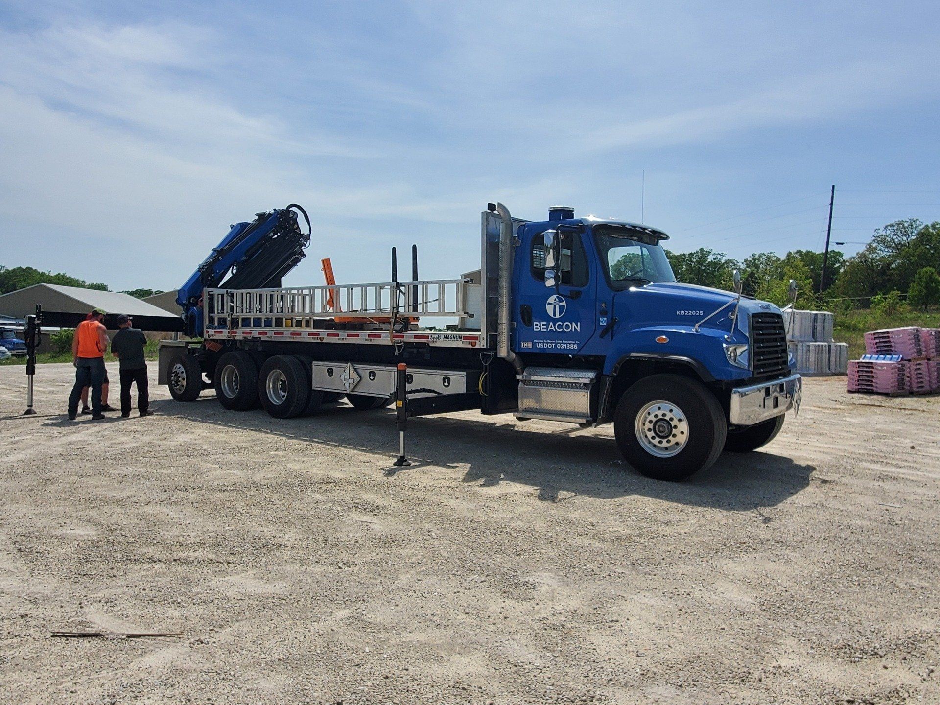 A blue truck with a crane on the back is parked in a dirt lot.