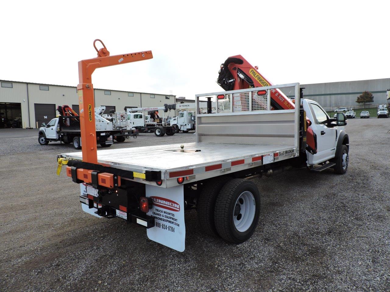 A flatbed truck with a crane on the back is parked in a gravel lot.