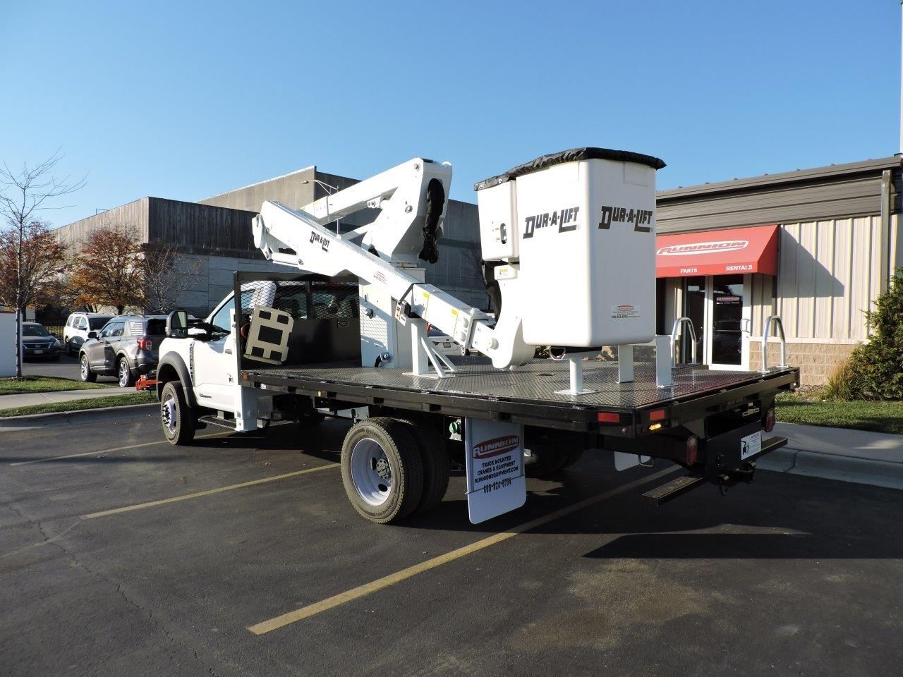 A white truck with an aerial lift on the back is parked in a parking lot.