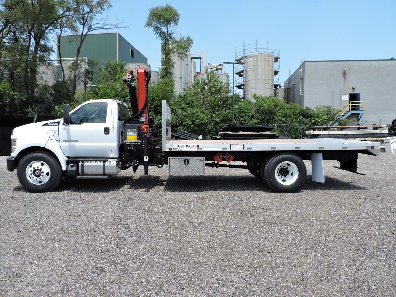 A flatbed tow truck with a crane on the back is parked in a gravel lot.