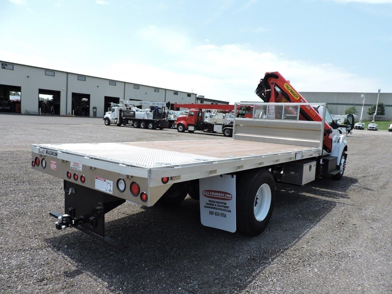 A flatbed truck with a crane on the back is parked in a parking lot.