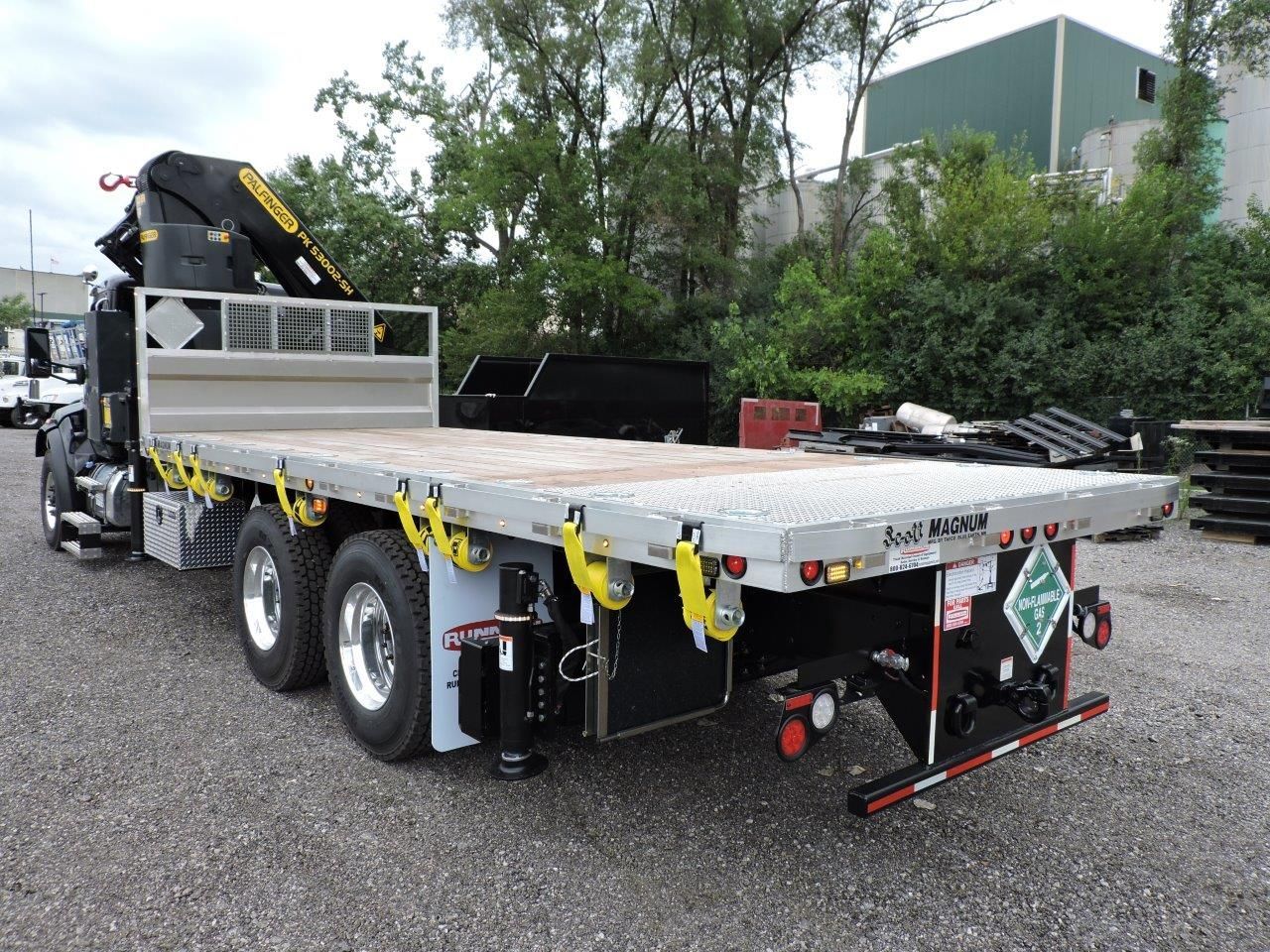 A flatbed truck with a crane on the back is parked in a gravel lot.