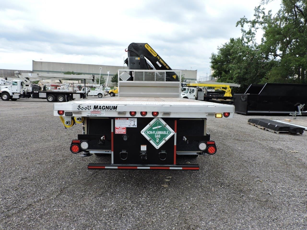 A flatbed truck with a crane on top is parked in a gravel lot.