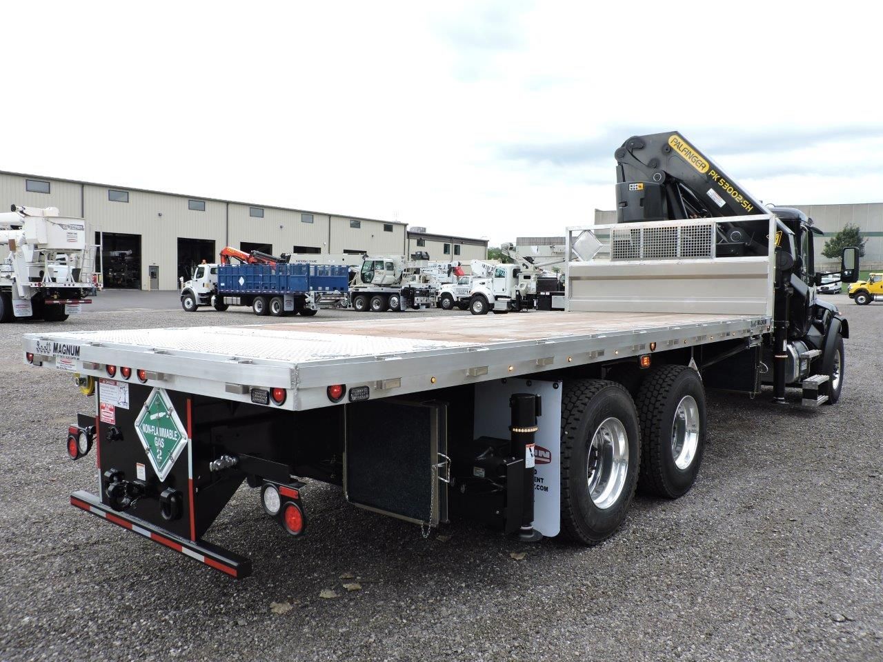 A flatbed truck with a crane on the back is parked in a gravel lot.